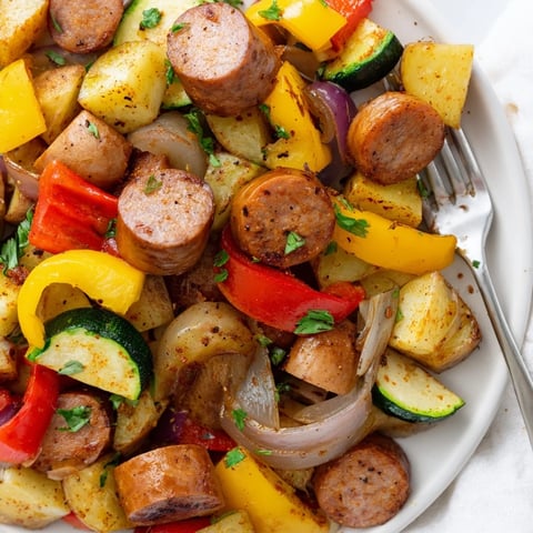 Saftige Bratwürste mit buntem Gemüse in einer rustikalen Pfanne serviert.  